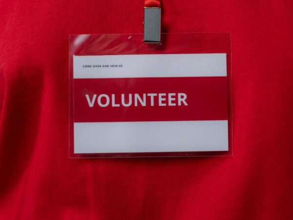 red name badge with the word volunteer and a space for a person's name Photo by cottonbro studio: https://www.pexels.com/photo/close-up-photo-of-a-volunteer-id-6565756/