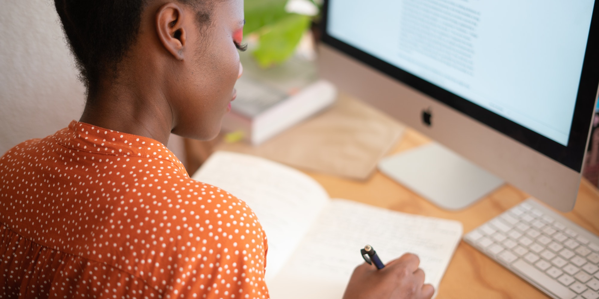 woman wearing orange shirt and matching eye shadow sitting in front of computer writing notes in a journal