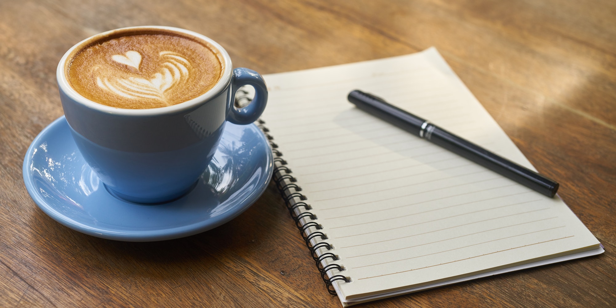 blue coffee cup with foam art heart beside a notebook and pen - Photo by Pixabay: https://www.pexels.com/photo/beverage-blue-breakfast-brown-414551/