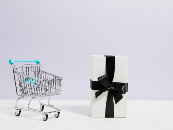 mini shopping cart next to gift with black ribbon and bow Photo by Karolina Grabowska: https://www.pexels.com/photo/shopping-cart-next-to-a-gift-box-5632395/