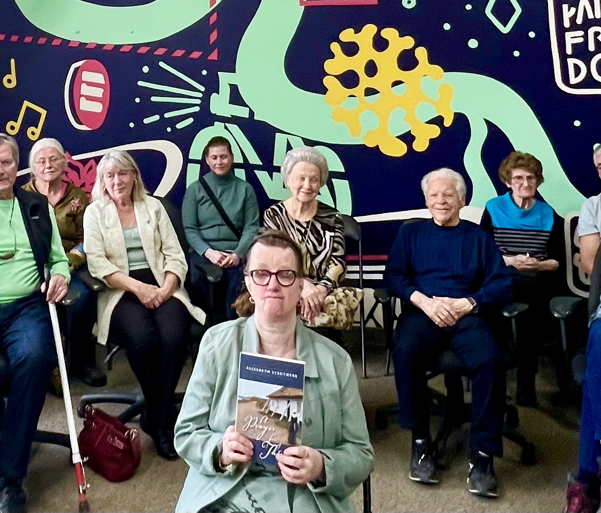 Elizabeth Struthers holds her book up in front of the audience as the group poses for photo during the book launch