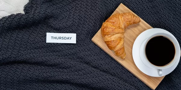 white tile with the word Thursday on a dark knit blanket next to a small wooden board with a croissant and a cup of black coffee Photo by cottonbro studio: https://www.pexels.com/photo/brown-bread-on-black-textile-3945214/