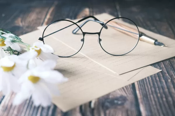 round, dark-rimmed spectacles and white daisies atop loose sheets of line paper on a worn wooden desk Photo by Towfiqu barbhuiya: https://www.pexels.com/photo/round-eyeglasses-on-white-paper-beside-daisies-9821383/