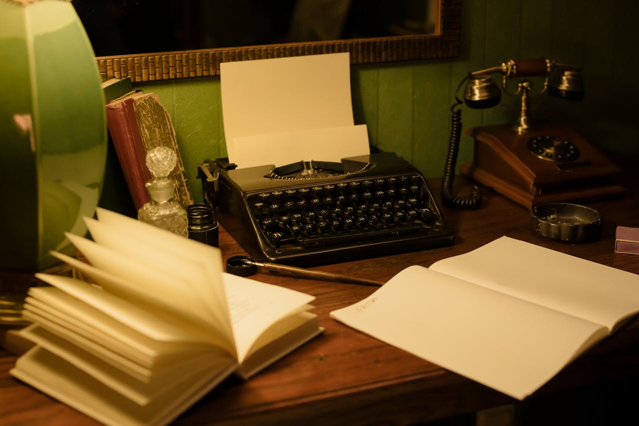 wooden desk with antique typewriter, writing instruments, and notebooks on surface Photo by cottonbro studio: https://www.pexels.com/photo/vintage-typewriter-and-telephone-on-the-table-7610808/